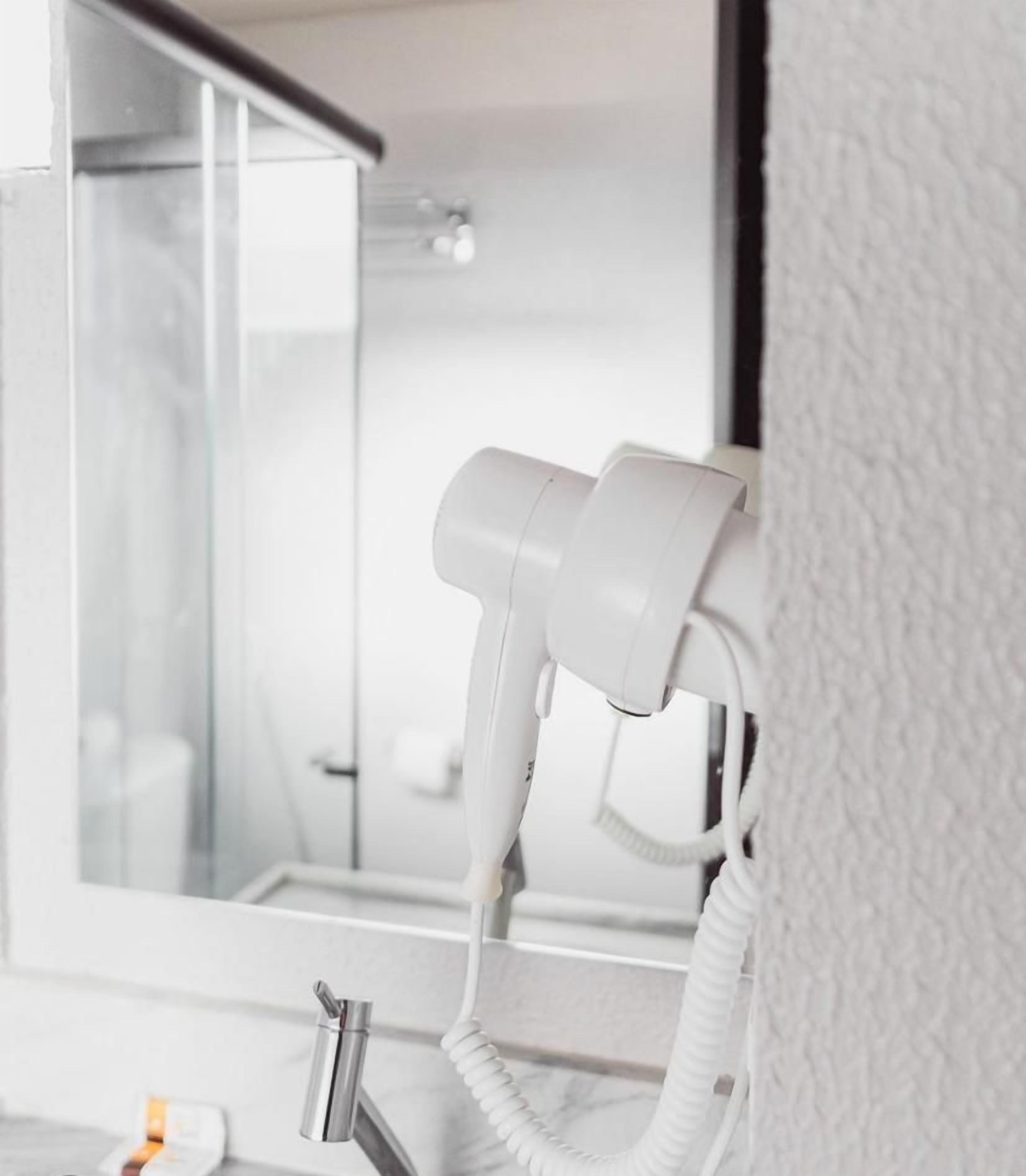 Une salle de bain moderne équipée d’un sèche-cheveux fixé au mur, d’une douche en verre et d’un distributeur de serviettes visible.