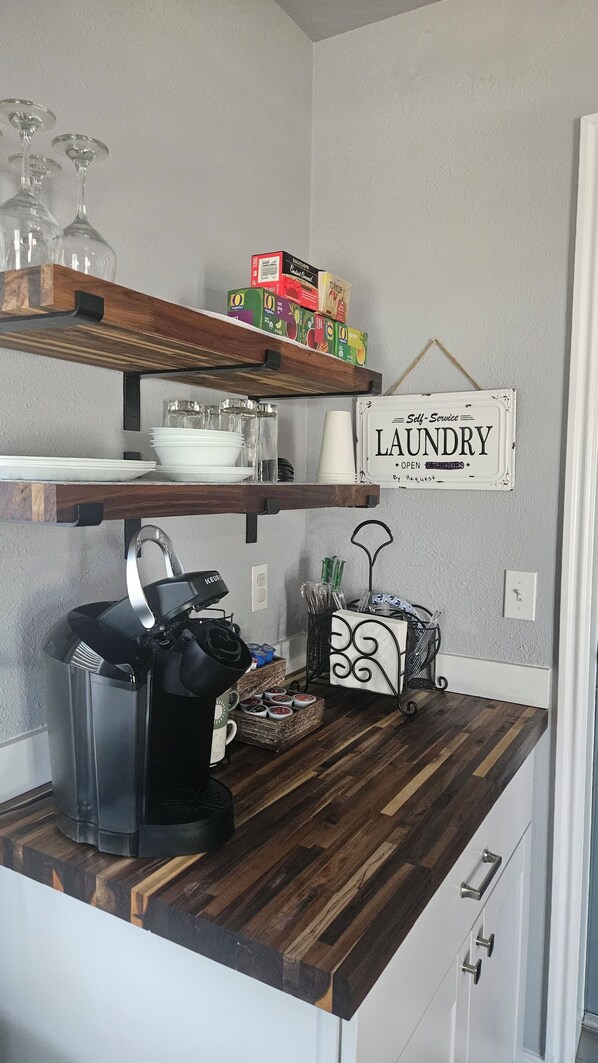A kitchen with wooden countertops, a coffee maker, a kettle, and a sign that says 'Laundry Open'.