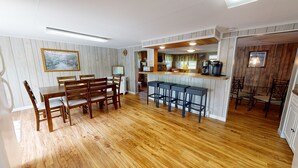 Een keuken met houten vloer, een eethoek met een tafel en stoelen, een bar met krukken, en een keukentoog met apparatuur.