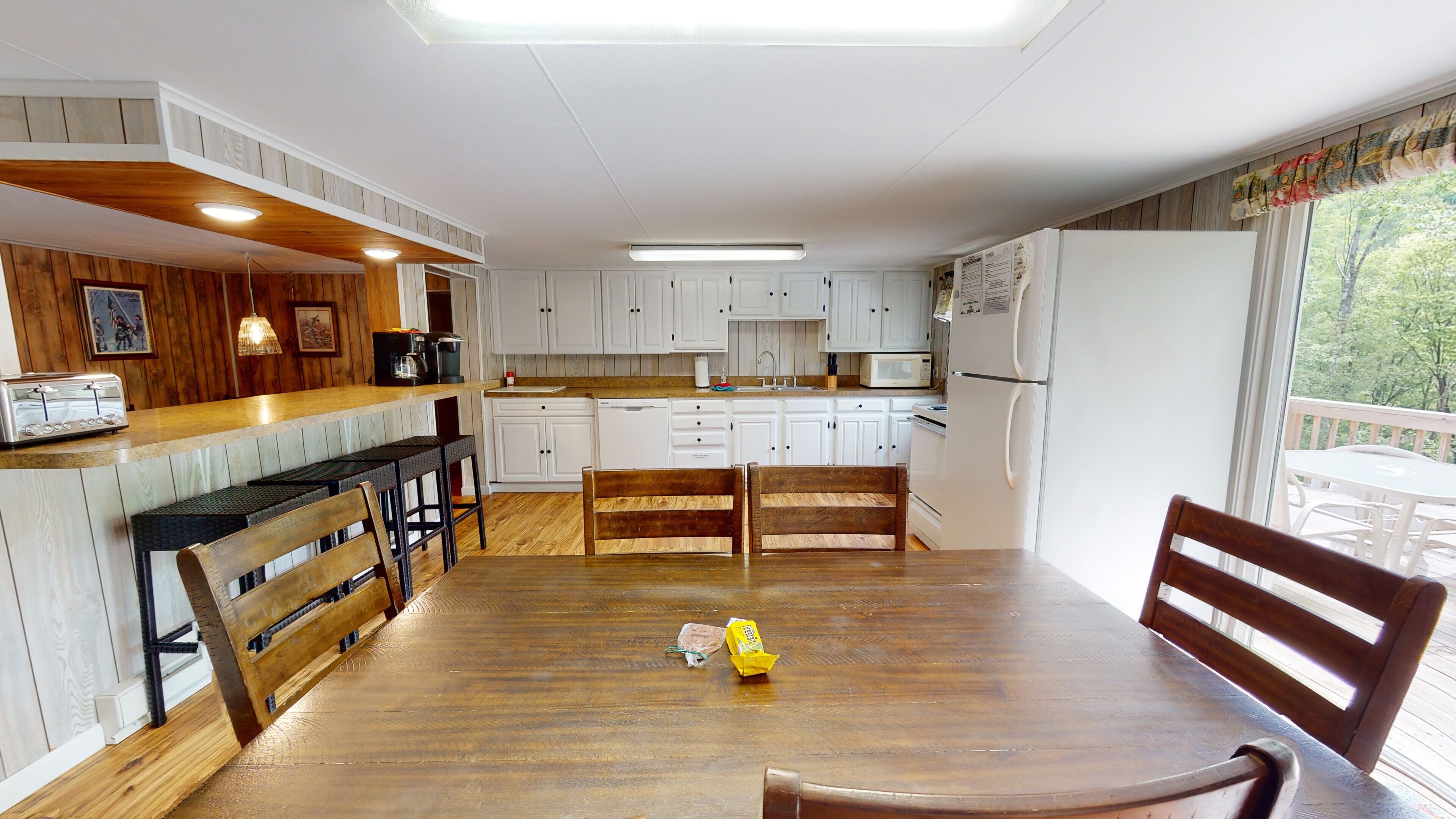 A kitchen with white cabinets, a wooden dining table, and a view of the outdoors.