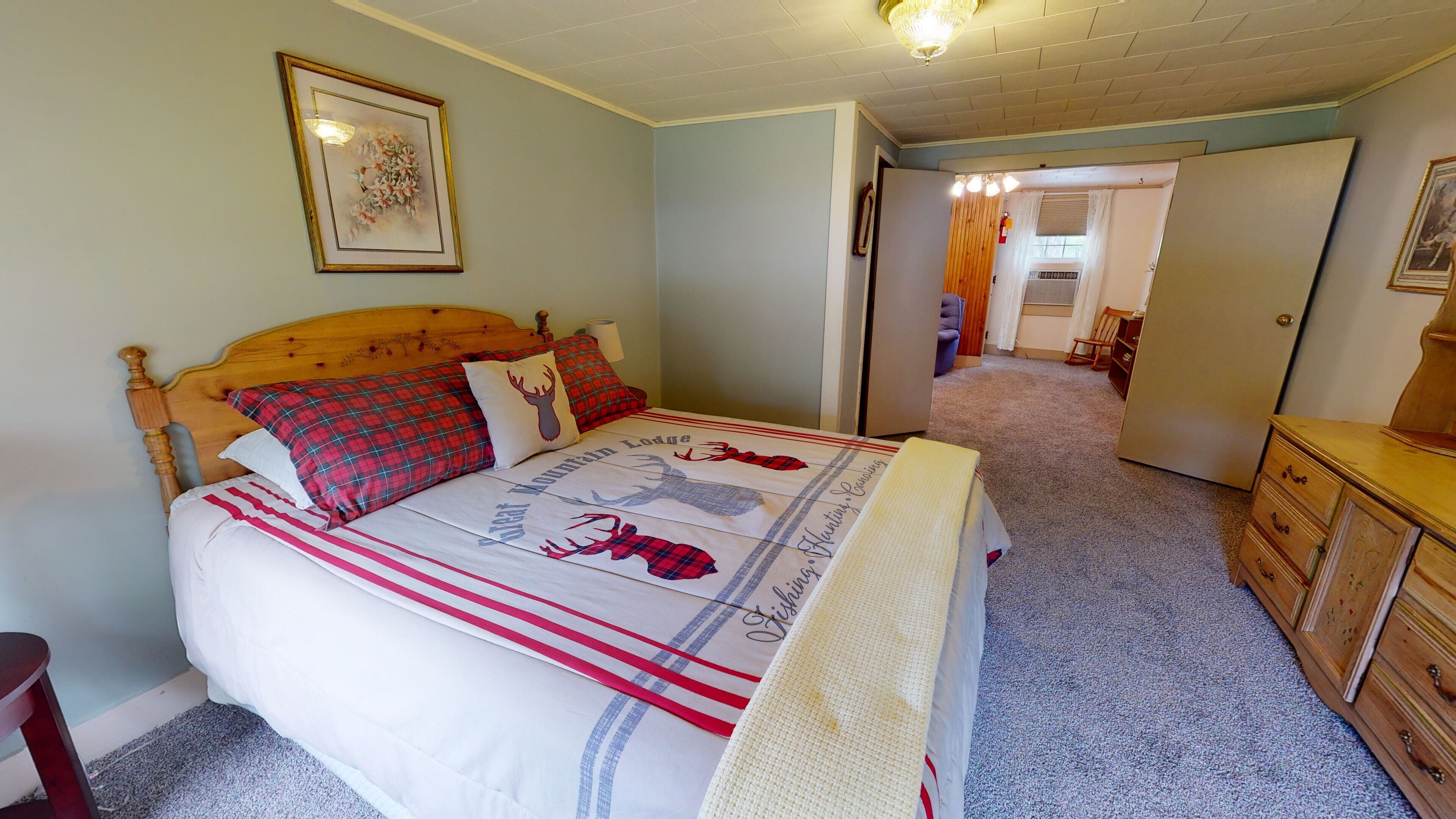 A bedroom with a bed, a dresser, and a door leading to another room.