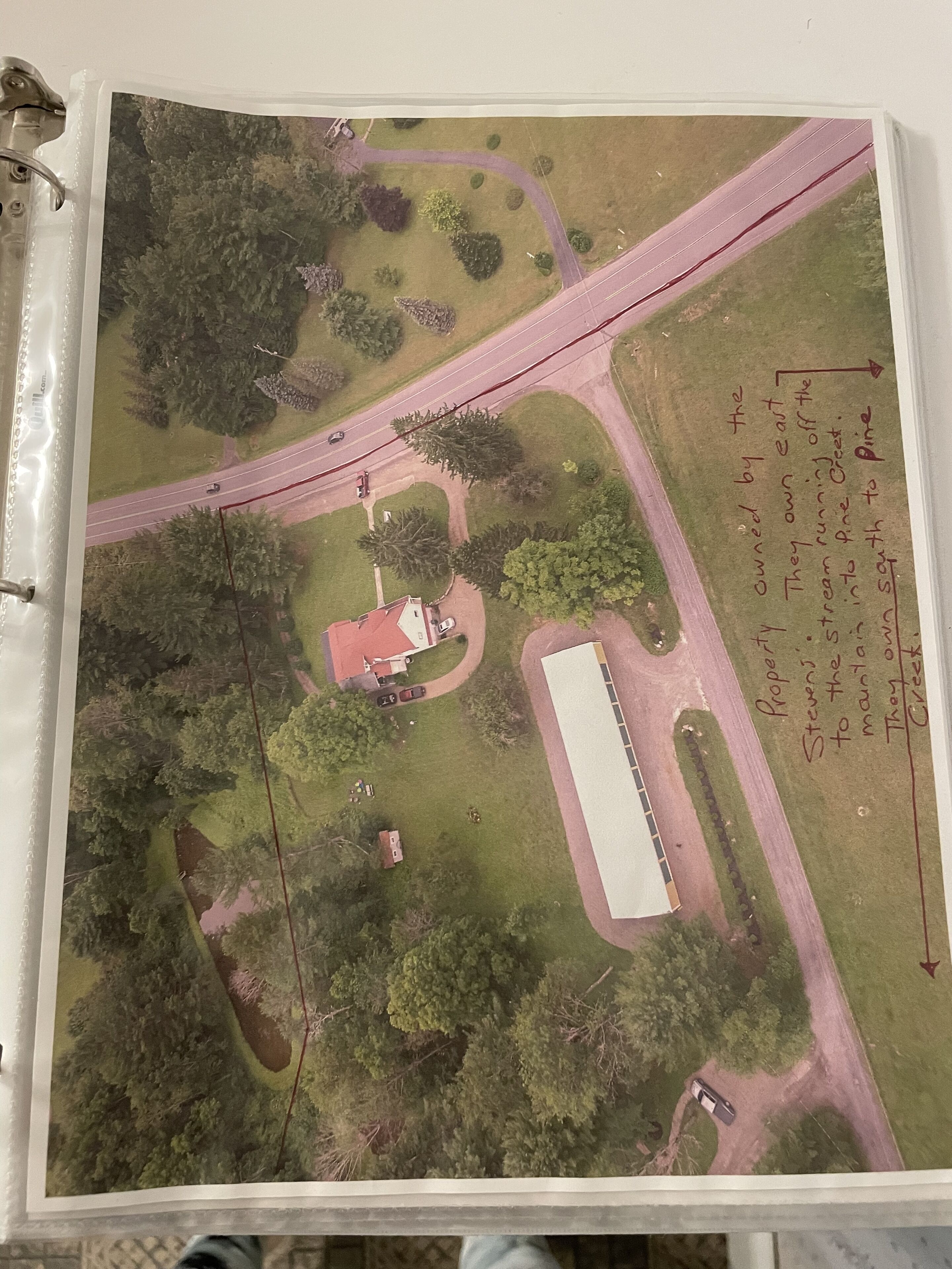 An aerial view of a property with a main building, a large open field, and a road.