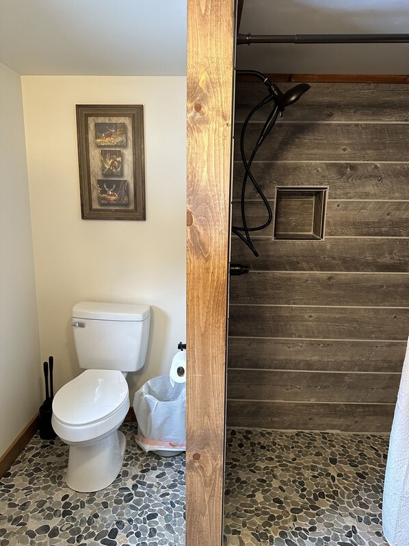 Un baño con inodoro, un cuadro en la pared y un revestimiento de madera con una pequeña ventana y una tubería.