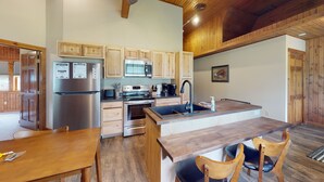 A modern kitchen with wooden cabinets, stainless steel appliances, and a wooden dining table with chairs. - Escape to Pine Creek and PA Grand Canyon stay at Willow Cabin (Gaines)