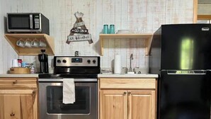 A kitchen with wooden cabinets, a stainless steel oven, a black refrigerator, and a microwave on a shelf. - Cozy Tiny Home Cabin Near Lake Greeson & Kirby Landing – Pet-Friendly! (Kirby)