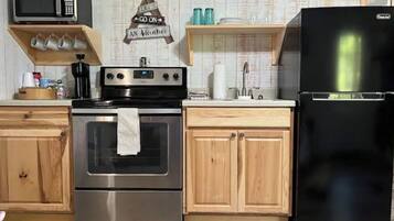 A kitchen with wooden cabinets, a stainless steel oven, a black refrigerator, and a microwave on a shelf.