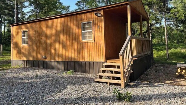 A small wooden cabin with a porch and a staircase leading to the entrance. - Cozy Tiny Home Cabin Near Lake Greeson & Kirby Landing – Pet-Friendly! (Kirby)