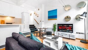 Ett modernt vardagsrum med en soffa, ett soffbord, en tv och en trappa som leder upp till ett kök.