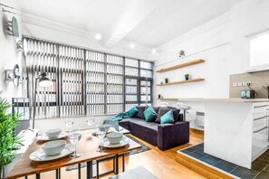 Une cuisine moderne dotée d’un îlot central, un coin repas avec une table dressée pour quatre personnes et un salon avec un canapé.