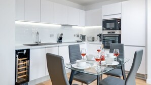 Une cuisine moderne avec des meubles blancs, un four encastré et un coin repas comprenant une table et des chaises en verre.