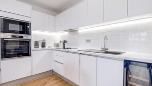 Una cocina moderna con armarios blancos, horno empotrado, cafetera y pileta de acero inoxidable.