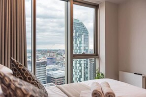 Habitación de hotel con un amplio ventanal que ofrece vistas a la ciudad, una cama bien hecha y un diseño moderno.
