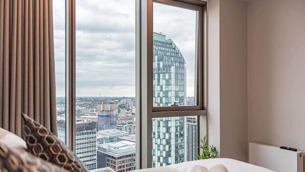 A hotel room with a large window offering a city view, a neatly made bed, and a modern design. - The Lexington III 2BDR | Games Room | Netflix (Merseyside)