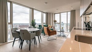 A modern living room with a dining area, large windows, and a city view. - The Lexington III 2BDR | Games Room | Netflix (Merseyside)