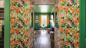 A hallway with floral wallpaper, a dining area with a table and chairs, and a window with curtains.