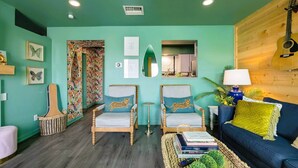 A living room with teal walls, two armchairs, a blue sofa, a guitar, and a lamp.