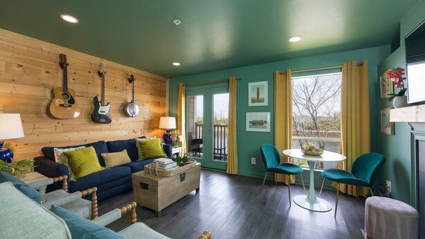A cozy living room with a wooden wall, a blue sofa, a coffee table, and a dining area with teal chairs and a white table.