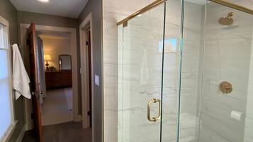 Een moderne badkamer met een glazen douchecabine, een zichtbaar toilet en een handdoek aan een deur.