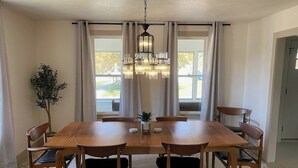 Comedor con mesa y sillas de madera, una araña y vistas al exterior a través de amplias ventanas.
