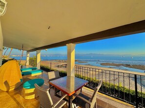 A balcony with wicker furniture, a glass table, and a view of the sea and distant mountains. - Villa Familiar Frente al mar (Cruz de Huanacaxtle)