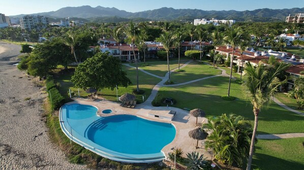A resort with a large swimming pool, palm trees, and a view of mountains. - Villa Familiar Frente al mar (Cruz de Huanacaxtle)
