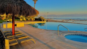 An infinity pool with a view of the ocean, a thatched umbrella, and lounge chairs. - Villa Familiar Frente al mar (Cruz de Huanacaxtle)