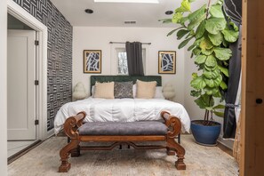 A bedroom with a bed, bench, potted plant, and two framed artworks.