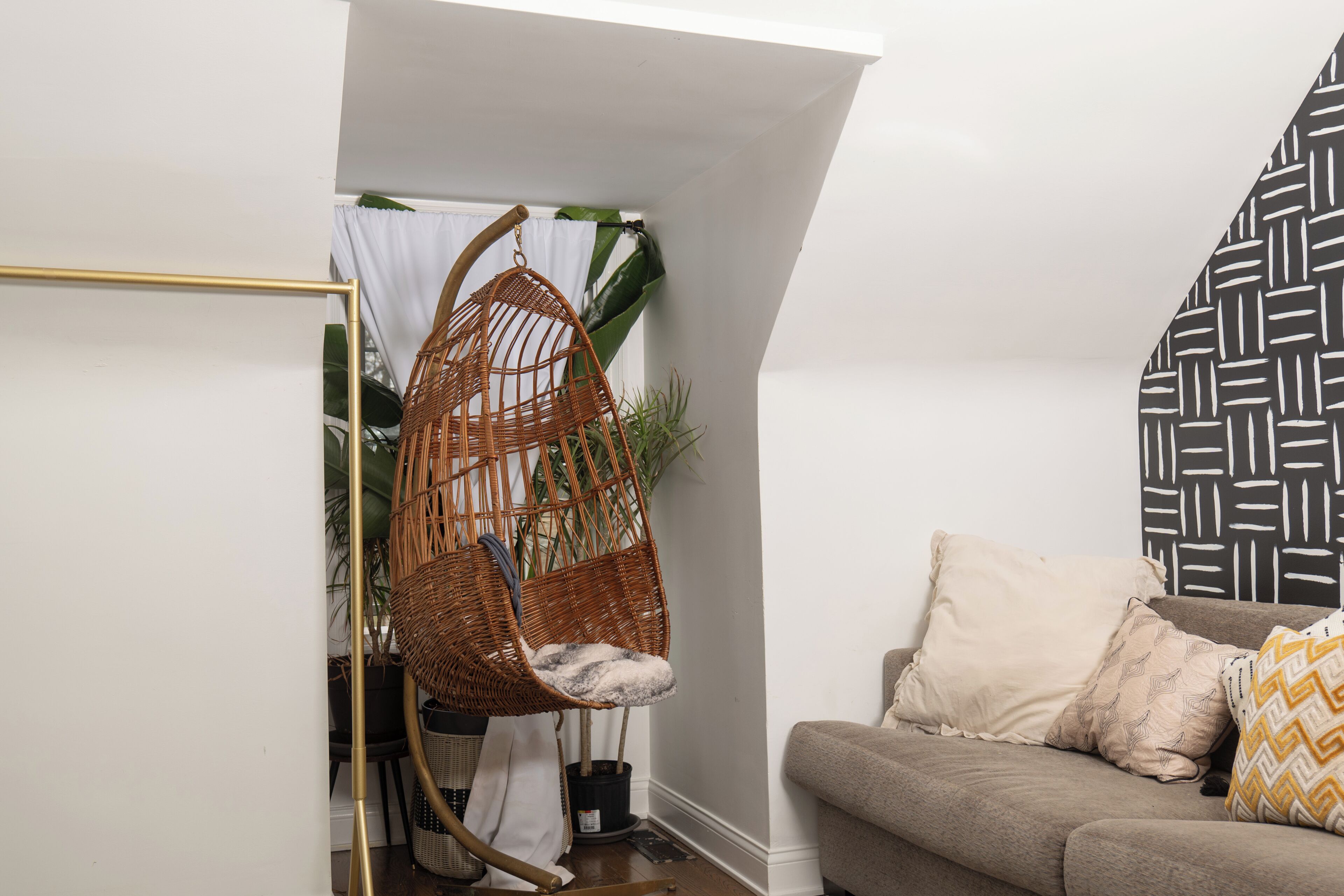 Una habitación con una silla de mimbre, un sofá con cojines estampados y una pared con diseño blanco y negro.