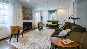 Un salón amplio con chimenea, un sofá verde, un sillón estampado y una mesa de centro.