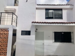A white building with a balcony, a door, and a window with a curtain.