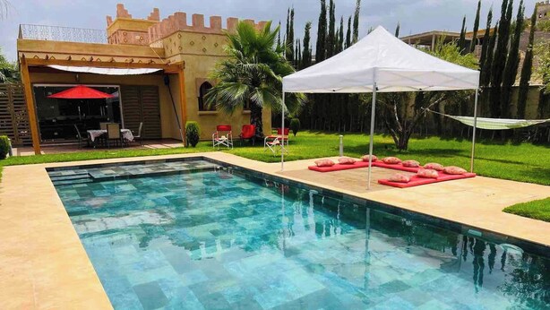 A rectangular swimming pool with clear blue water, surrounded by a tiled deck. There are red lounge chairs and a white canopy tent. - Private Villa With Swimming Pool in Lalla Takerkousst-marrakech (Lalla Takarkoust)