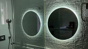 A bathroom with a glass shower enclosure, a marble sink, and two round mirrors with illuminated frames. - Private Villa With Swimming Pool in Lalla Takerkousst-marrakech (Lalla Takarkoust)