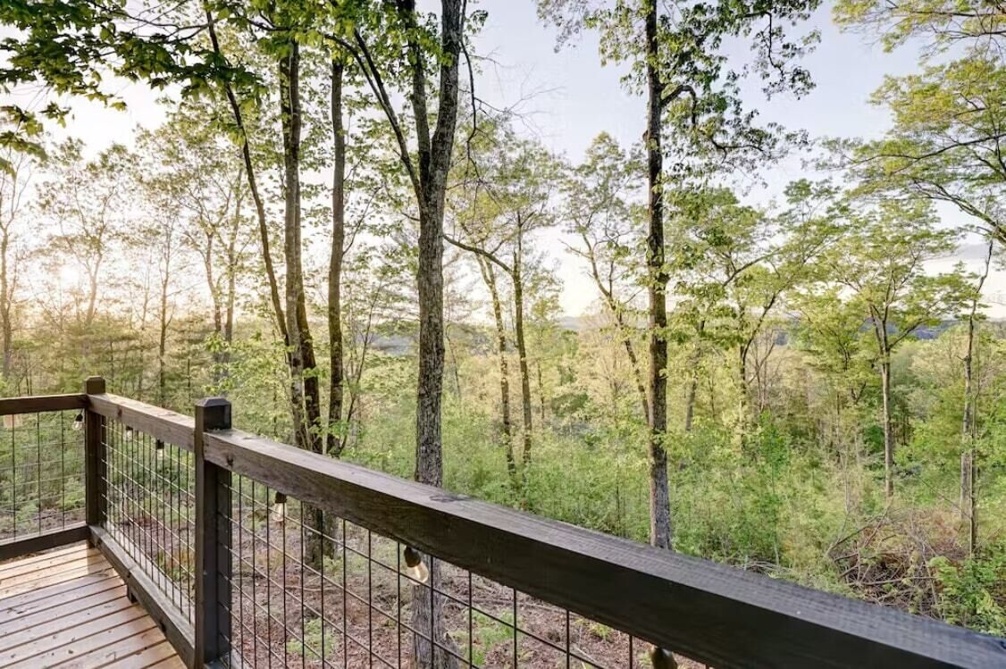Une terrasse en bois avec une rambarde en métal donnant sur une zone boisée.