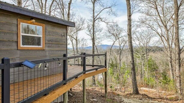 A wooden cabin with a deck and a window, surrounded by trees and mountains.