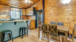 A wooden cabin interior with a kitchen, dining area, and a ceiling fan.