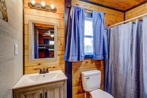 A wooden cabin bathroom with a sink, toilet, and window with curtains. - Hot Tub - Mountain View - Fire Pit - Gas Grill - Comfy Beds - Pet Friendly (Ellijay)