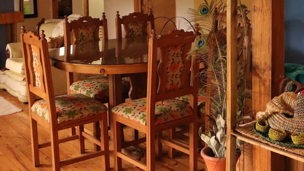 Un coin repas en bois avec une table et des chaises, une décoration en plumes de paon et un panier tressé posé sur une étagère.