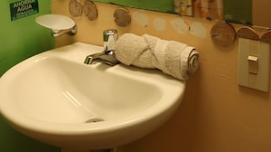 Une salle de bain avec un mur vert, un lavabo blanc, une serviette, un rideau de douche et deux distributeurs de savon pour les mains.
