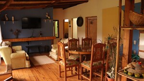 Un salon chaleureux avec une table à manger en bois, des chaises à motifs floraux, un téléviseur et des objets de décoration.