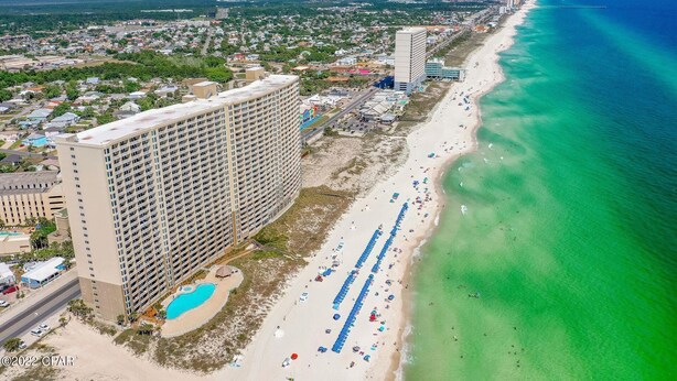 Eine Küstenstadt mit einem langen Strand, einem hoch aufragenden Hotel mit mehreren Etagen und einem klaren, blauen Meer.