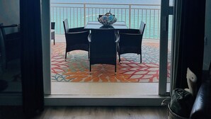 Ein Zimmer mit Meerblick durch eine Glastür, ein Tisch mit Stühlen und einem gemusterten Teppich.