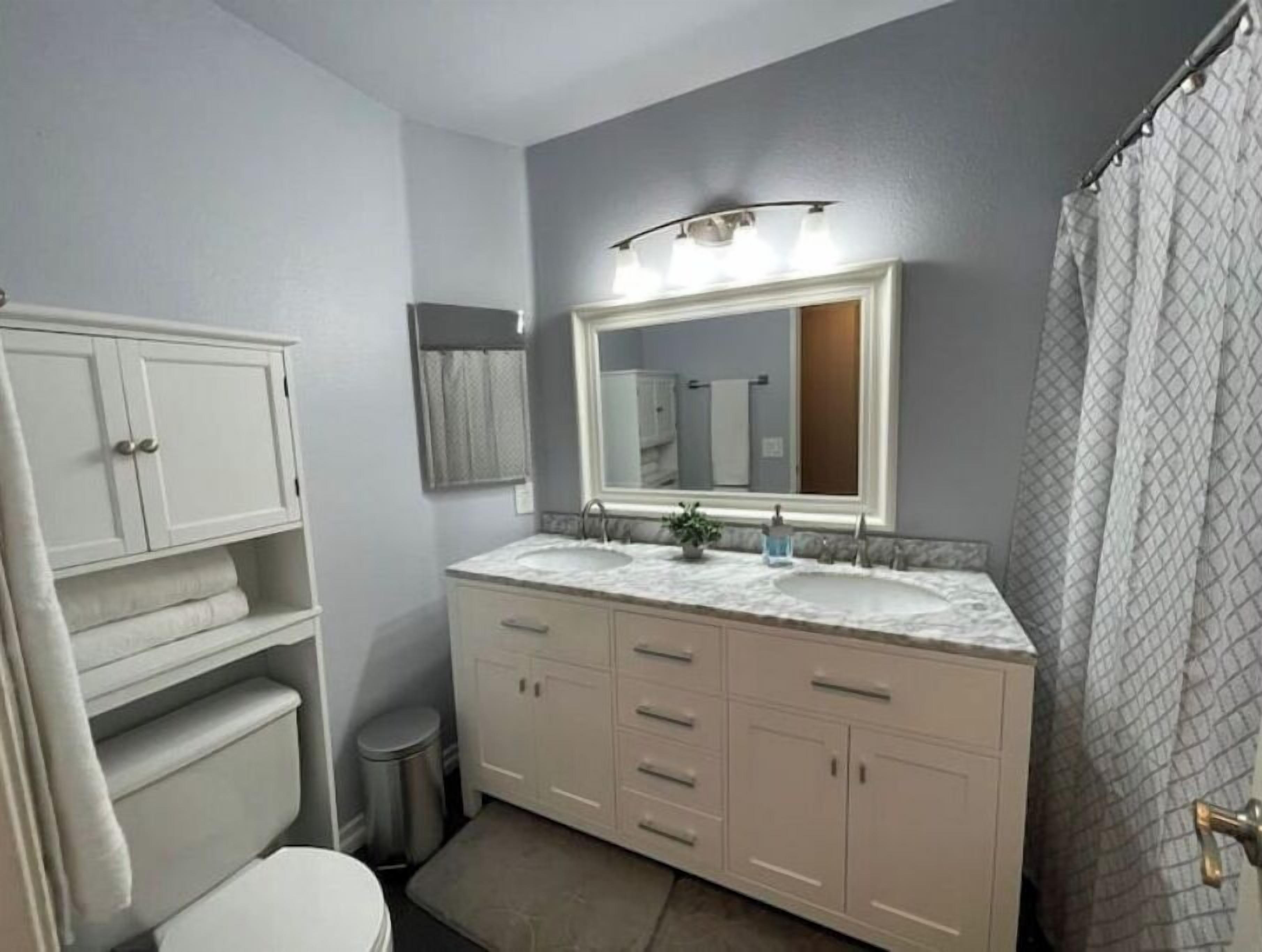 A bathroom with a white vanity, a double sink, a mirror, and a shower curtain.