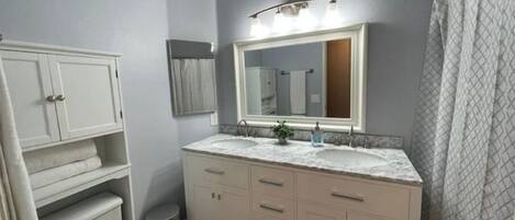 A bathroom with a white vanity, a double sink, a mirror, and a shower curtain.