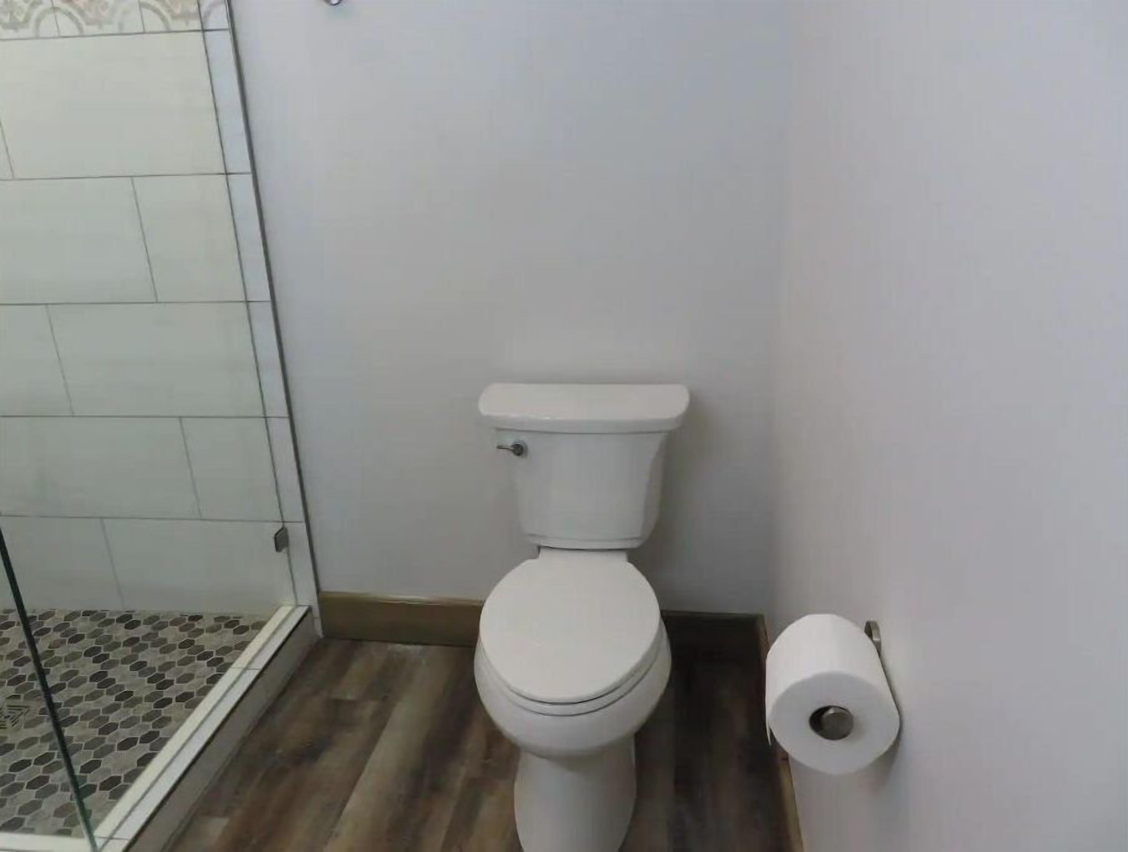 Une salle de bain comprenant des toilettes, un espace douche et un porte-rouleau de papier toilette.