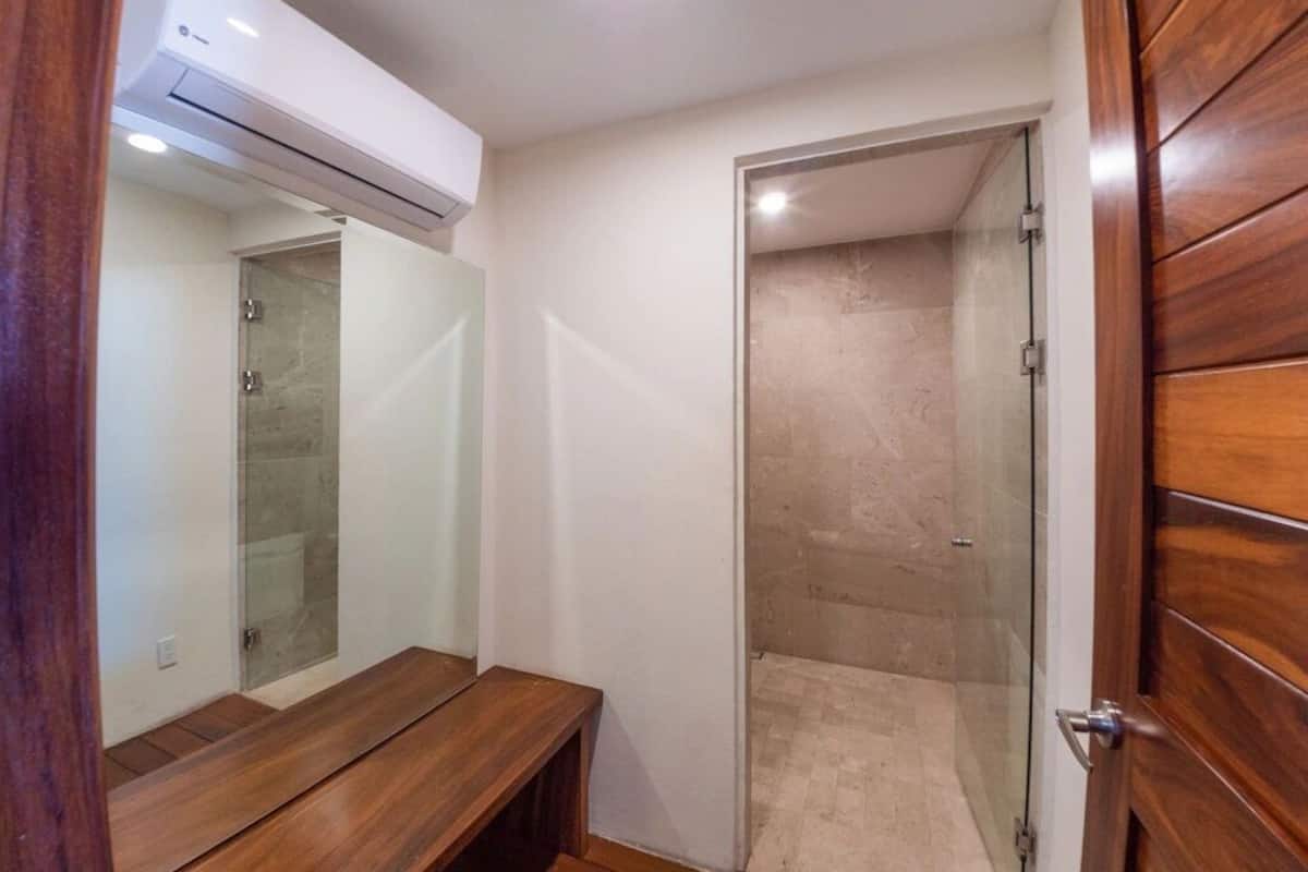 A bathroom with a wooden bench, a glass shower enclosure, and a wooden door.