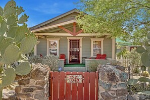 Una casa con un porche, un portón rojo y cactus.