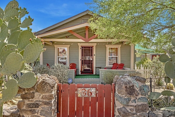 A house with a porch, a red gate, and cacti.