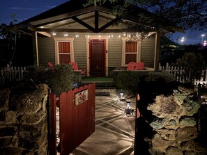 A house with a covered porch, two red chairs, a red door, and a stone wall with a gate.