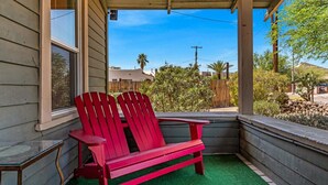 Une chaise Adirondack rouge et un banc sur une véranda, avec vue sur une clôture en bois et de la verdure.