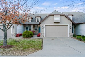 A two-story house with a garage, a front porch, and a tree with autumn leaves.